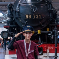 Ein Junge steht salutierend vor einer großen Lokomotive.