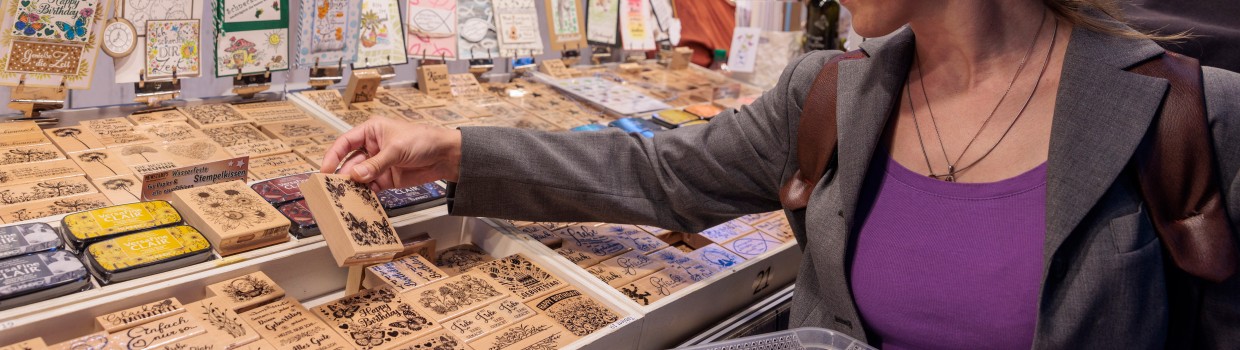 Eine Frau schaut sich das Sortiment eines Verkaufstandes an. Sie hält eine Holzschachtel in der Hand.