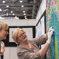 Eine Frau bastelt an einer Kunstwand. Eine weitere Frau schaut ihr dabei zu.