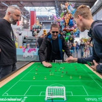 3 Männer stehen an einem Miniatur Fußballfeld.