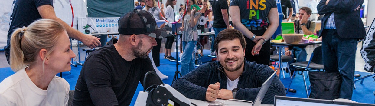 Einer Frau und eine Mann wird ein Roboterarm erklärt. Einer Frau und eine Mann wird ein Roboterarm erklärt.