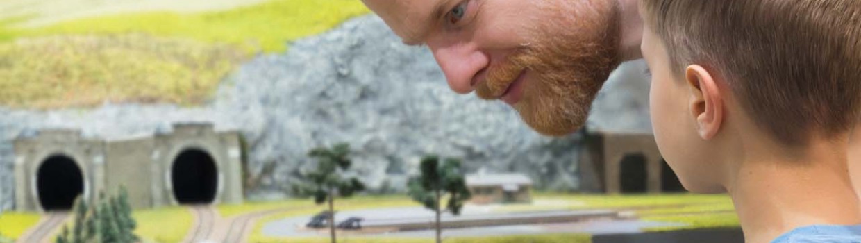 Zwei Personen schauen sich eine Modelleisenbahnstrecke auf der Hobbymesse Leipzig 2025 an, wo gerade eine Modelleisenbahn aus einem Tunnel fährt.