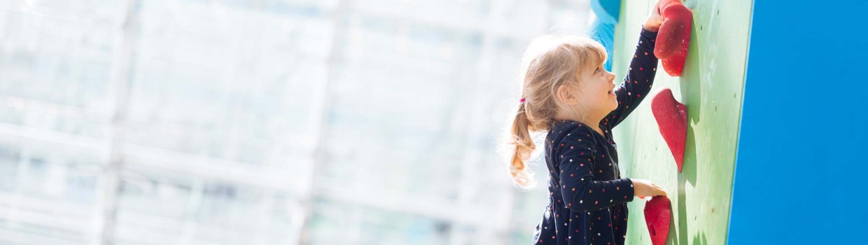 Eine Person hilft ihrem Kind auf der Hobbymesse Leipzig 2025 beim Klettern beziehungsweise Bouldern in der Glashalle der Leipziger Messe am Kletterturm.